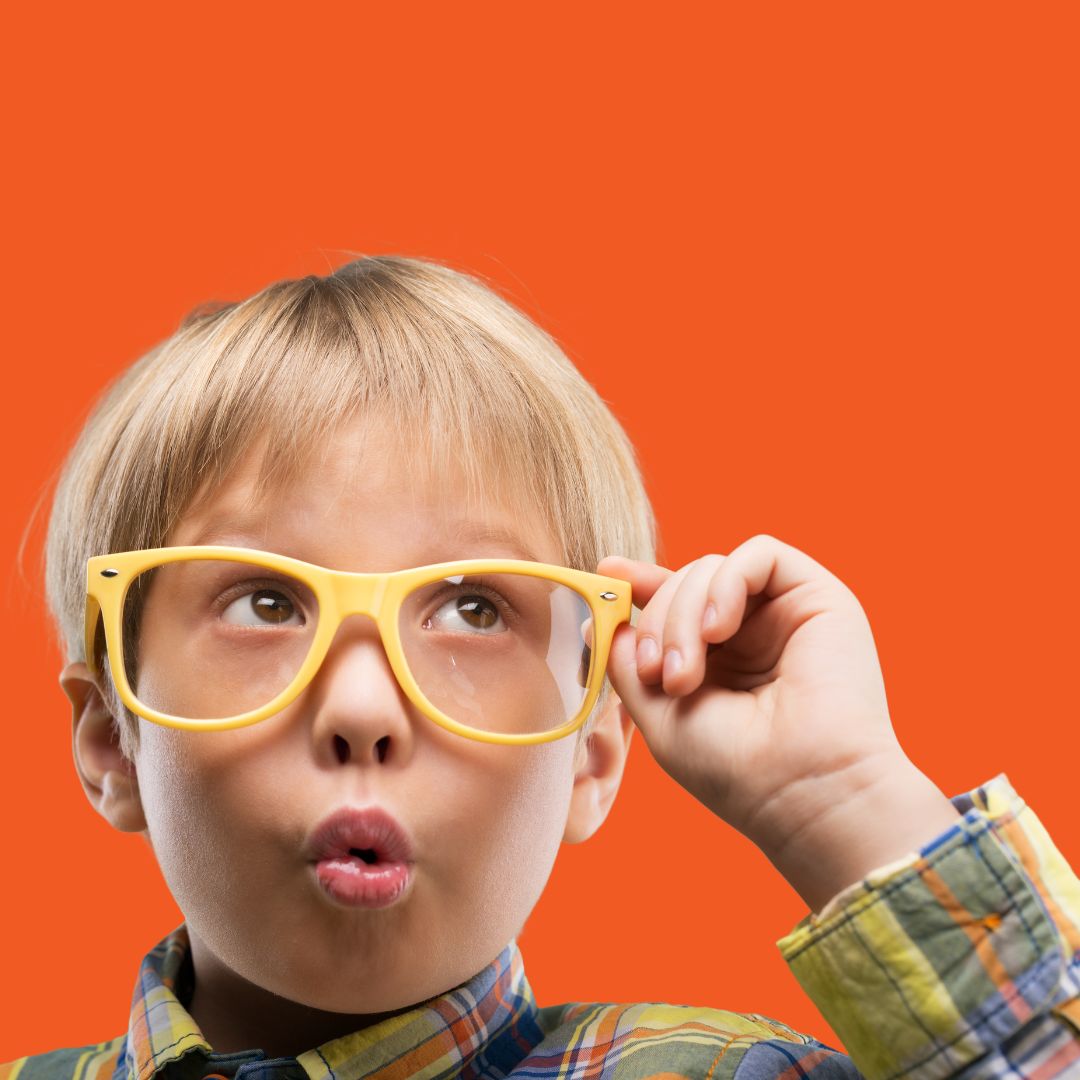 Curious blond kid in bright yellow glasses making an “ooh!” face while looking up, popping against an orange background.